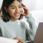 Hispanic woman working remotely on laptop near notepad in apartment