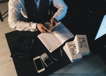 Businessman organizing finances with tech devices and cash on desk.