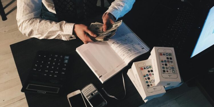 Businessman organizing finances with tech devices and cash on desk.