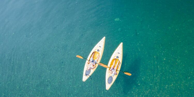 Aerial shot of two people kayaking on clear, turquoise water in a tranquil setting.