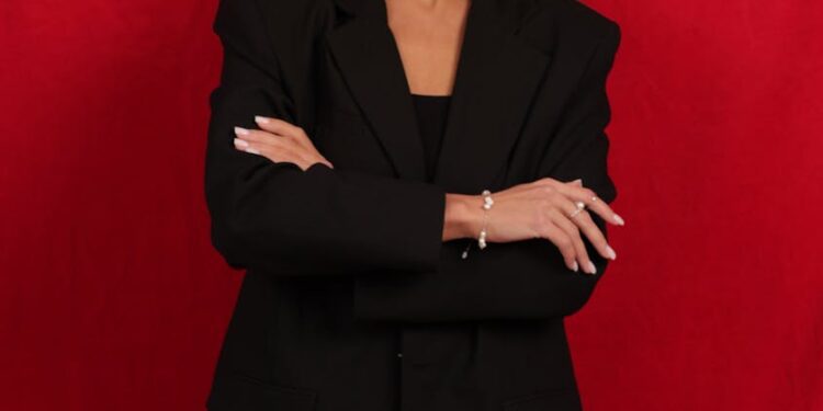 Elegant portrait of a woman in a black suit against a red background.