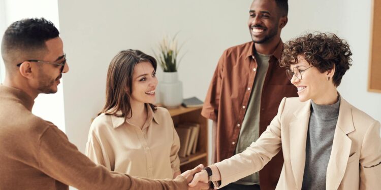 Four colleagues smiling and shaking hands in a bright office setting.