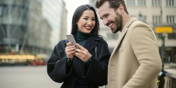 A happy couple shares a joyful moment in the city, interacting with a phone outdoors.