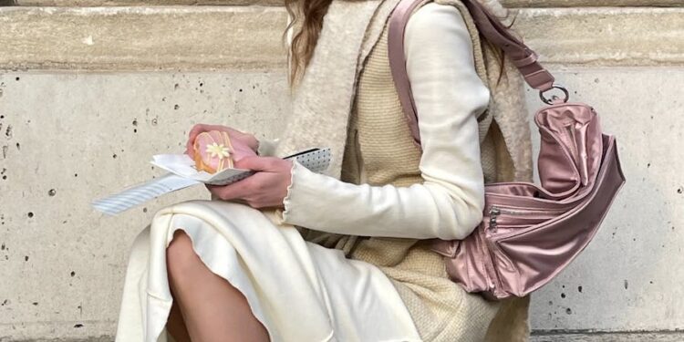 Stylish woman in fall fashion sitting outdoors with book and bag.