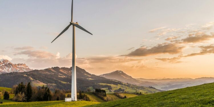 Wind turbine amid rolling hills and mountains at sunset, symbolizing renewable energy and sustainability.