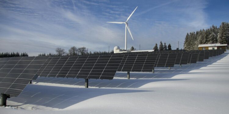 Solar panels and wind turbine in a snowy landscape, showcasing renewable energy sources.