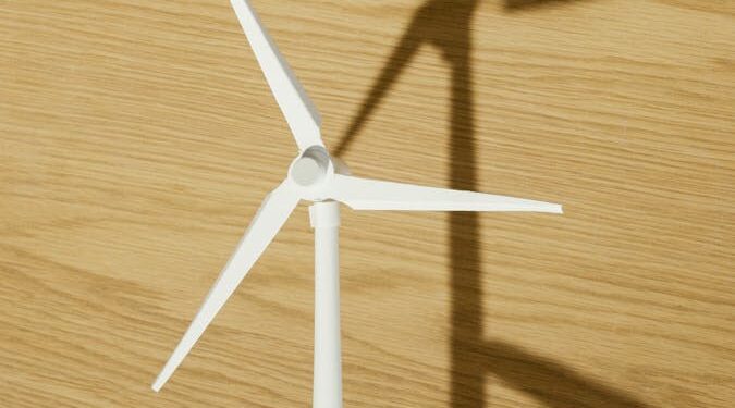 Close-up of a hand holding a small wind turbine model casting a shadow on a wooden surface.