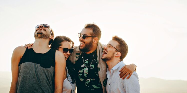 A group of young adults laughing and enjoying time together outdoors under the sun.