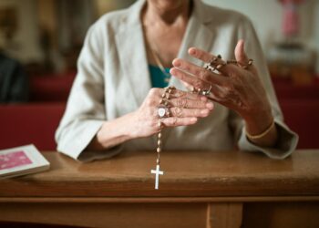 Close-up of a woman praying with a rosary in a church environment, symbolizing faith and spirituality.