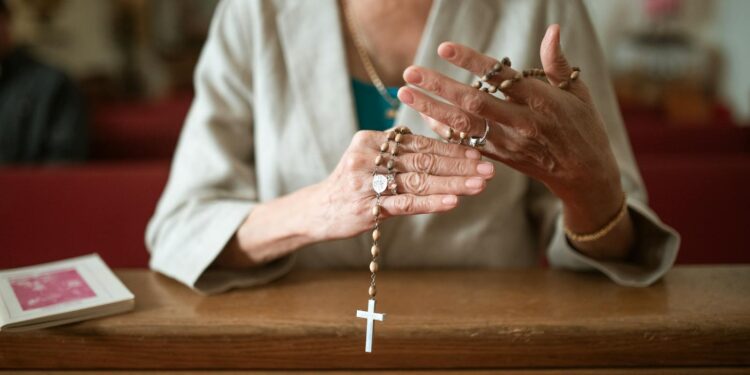 Close-up of a woman praying with a rosary in a church environment, symbolizing faith and spirituality.