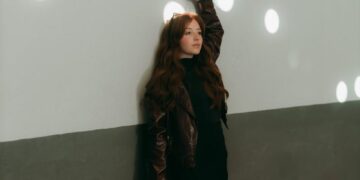 Fashionable woman poses against a wall with light spots indoors.