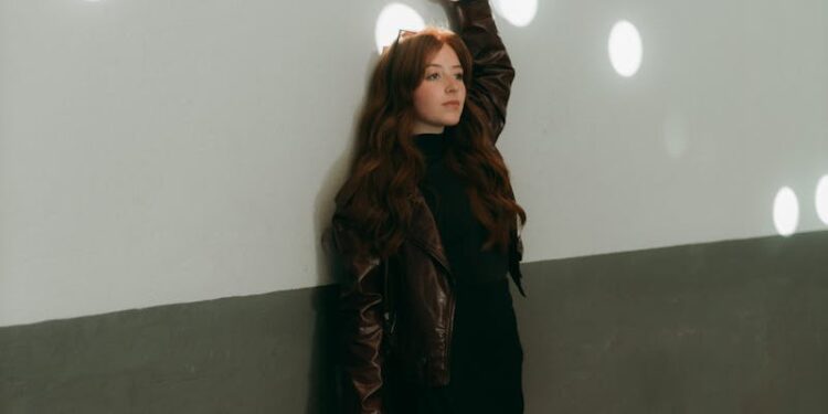 Fashionable woman poses against a wall with light spots indoors.
