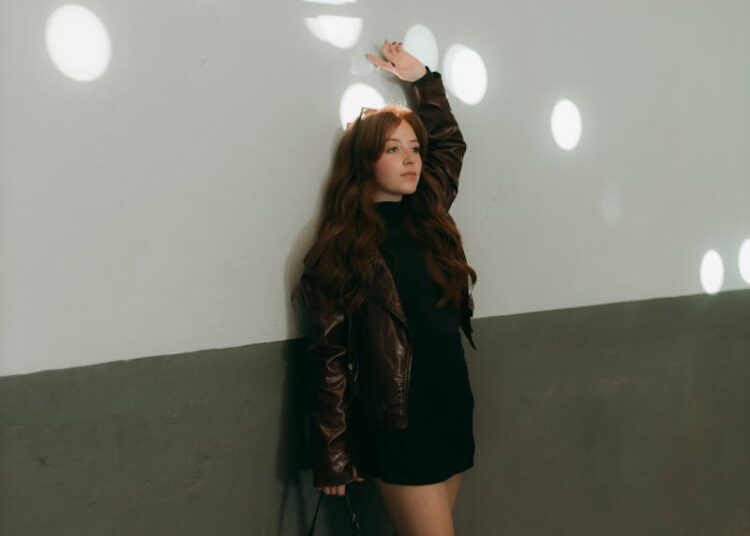 Fashionable woman poses against a wall with light spots indoors.