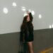 Fashionable woman poses against a wall with light spots indoors.