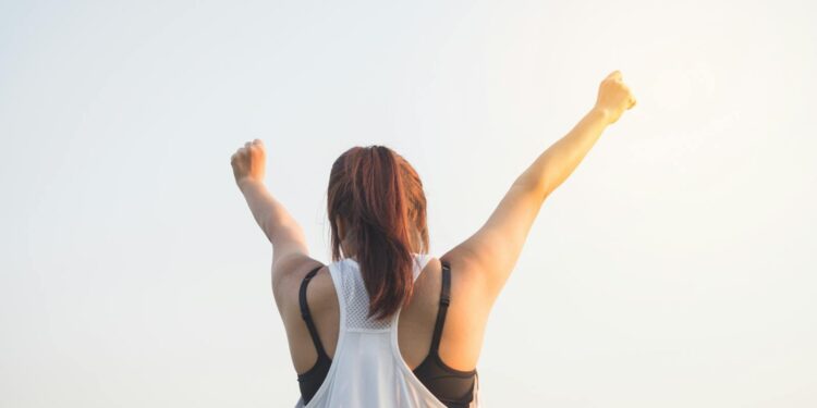 A woman celebrates success with arms raised in a bright outdoor setting.