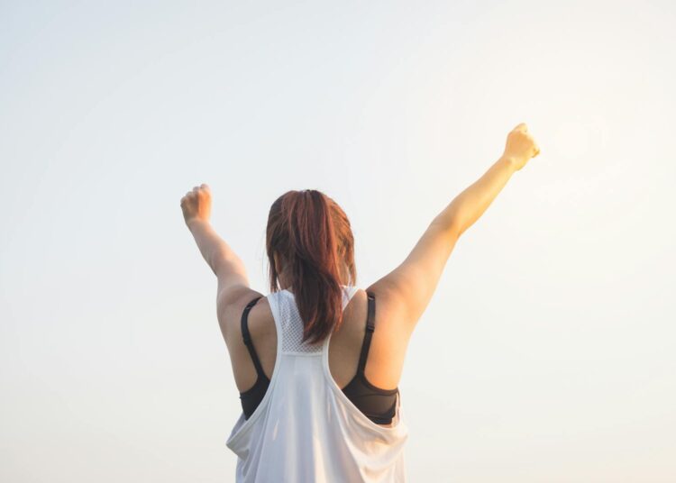 A woman celebrates success with arms raised in a bright outdoor setting.