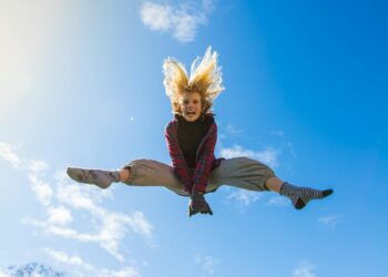 A girl energetically jumping under a clear blue sky, expressing freedom and joy.