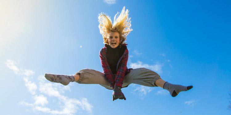 A girl energetically jumping under a clear blue sky, expressing freedom and joy.
