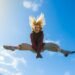 A girl energetically jumping under a clear blue sky, expressing freedom and joy.