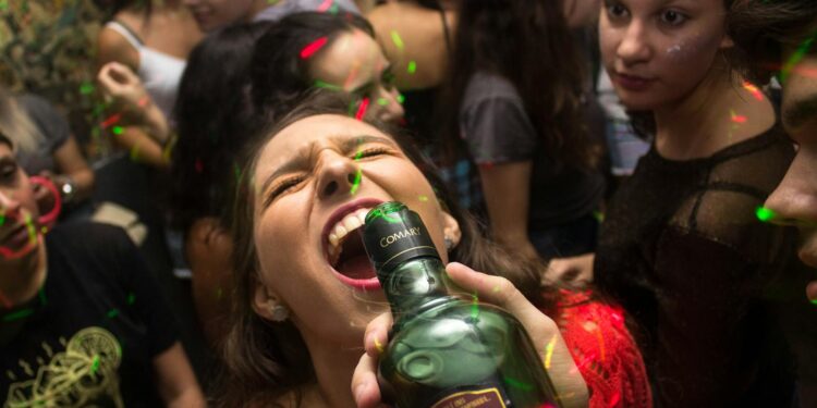 Exciting party scene with young adults enjoying drinks and dancing under colorful lights.