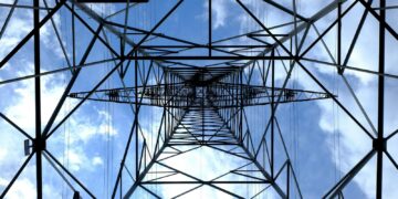 Looking up at a steel power pylon against a bright blue sky.
