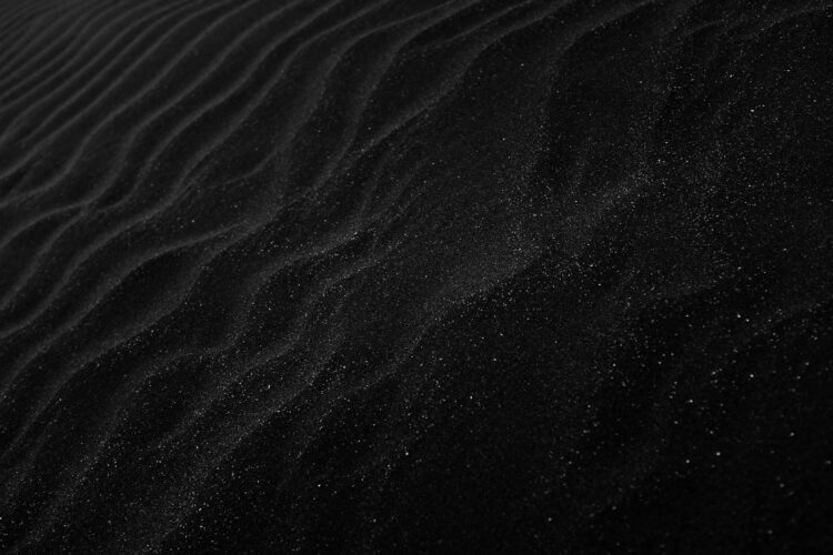 Textured black sand with ripples resembling dunes, creating a dark, abstract aesthetic.
