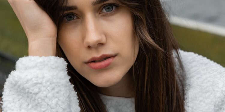 A young woman in a fluffy sweater poses thoughtfully outdoors in autumn.