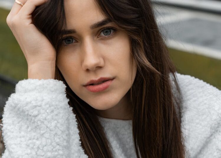 A young woman in a fluffy sweater poses thoughtfully outdoors in autumn.