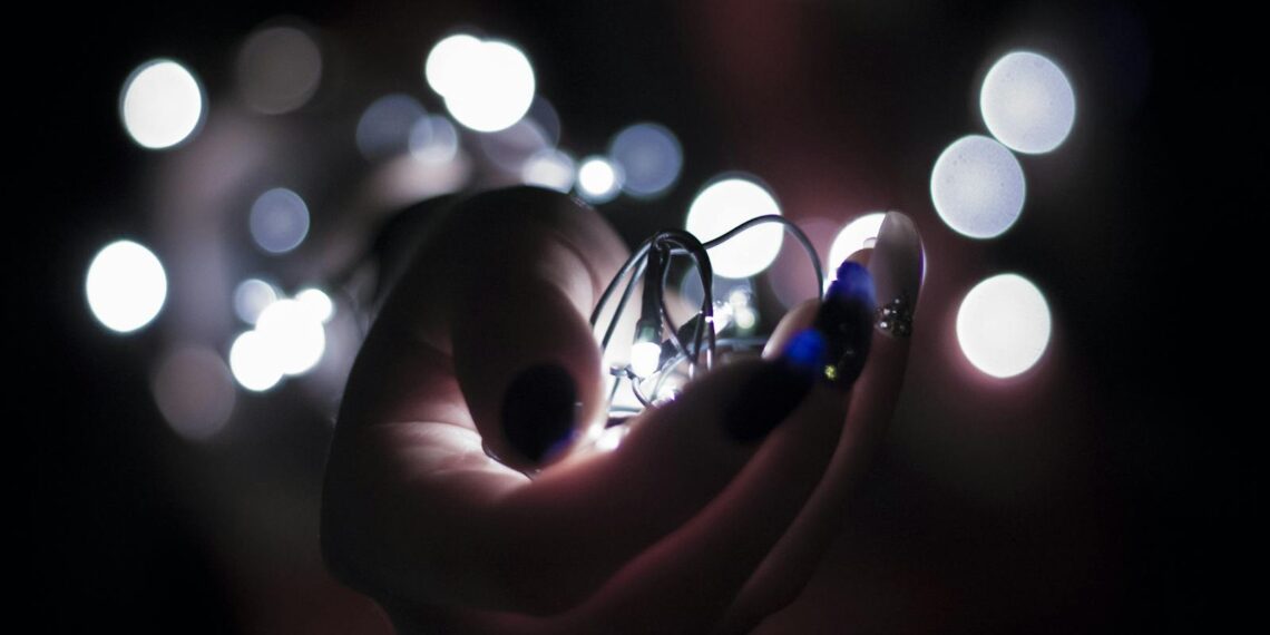Close-up of a hand holding glowing string lights with a bokeh effect, creating a festive atmosphere.