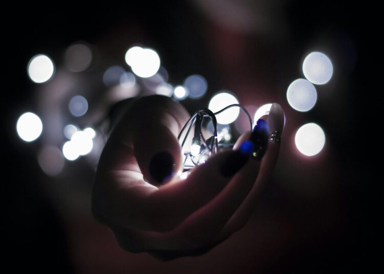 Close-up of a hand holding glowing string lights with a bokeh effect, creating a festive atmosphere.