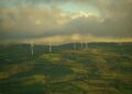 Wind turbines dotting a green, hilly landscape under cloudy sky