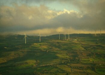 Wind turbines dotting a green, hilly landscape under cloudy sky