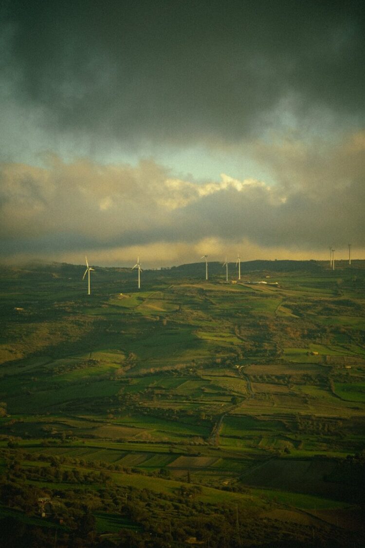 Wind turbines dotting a green, hilly landscape under cloudy sky