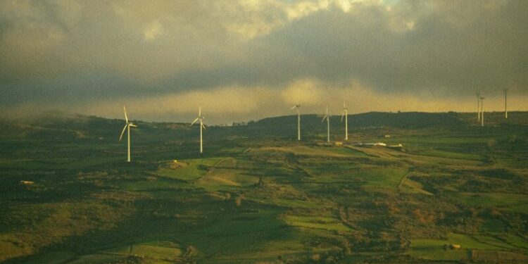 Wind turbines dotting a green, hilly landscape under cloudy sky