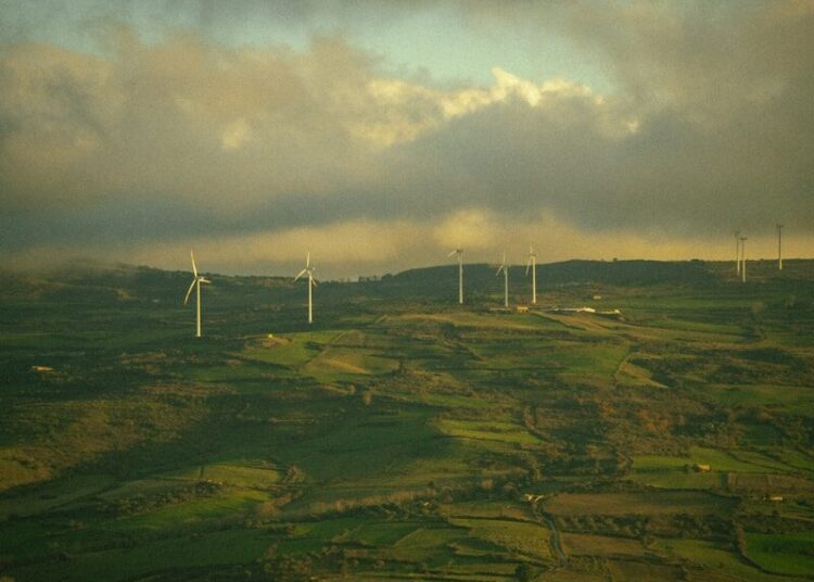 Wind turbines dotting a green, hilly landscape under cloudy sky