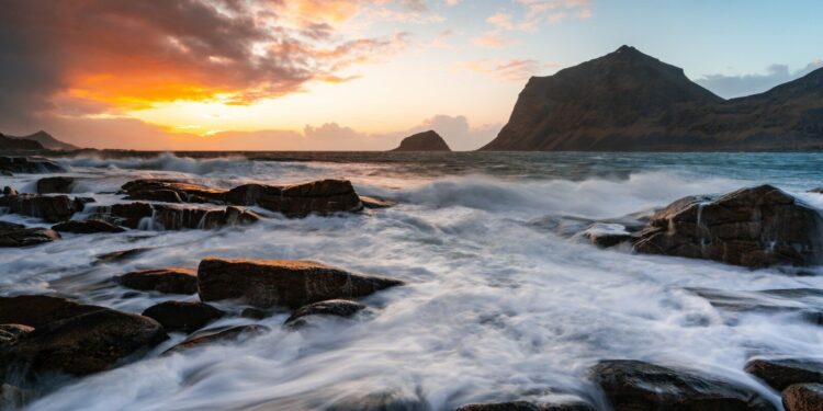 Vibrant sunset illuminates ocean waves crashing on a rocky shore.