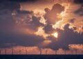 Wind turbines in the ocean under a cloudy sky with low golden light