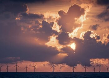 Wind turbines in the ocean under a cloudy sky with low golden light