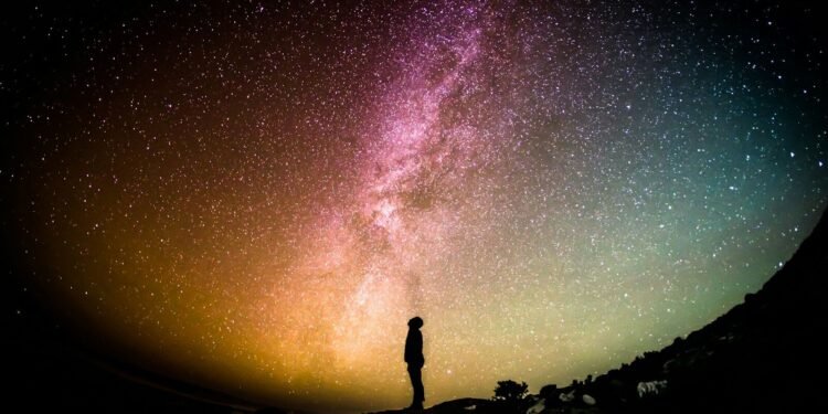 A lone silhouette standing under the Milky Way, dwarfed by the vastness of space