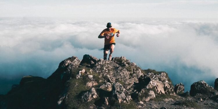 Trail runner reaching a mountain summit above the clouds, a comeback story