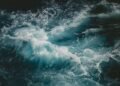Teal wave crashing in a dark sea