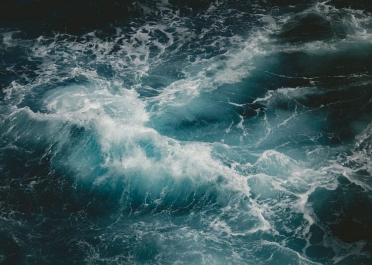 Teal wave crashing in a dark sea