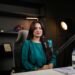 Smiling woman newscaster in a television news studio, placeholder for the Good News host