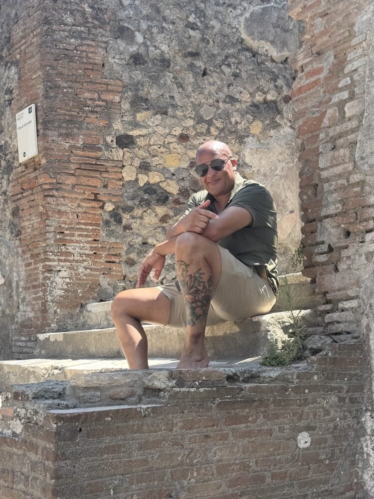 Phil smiling in sunglasses while sitting on old brick steps