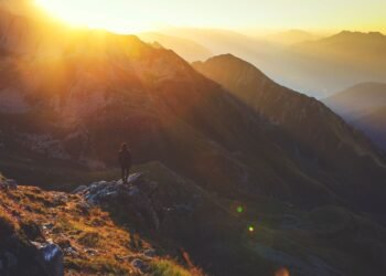 A lone hiker on a rocky mountain ridge at sunrise