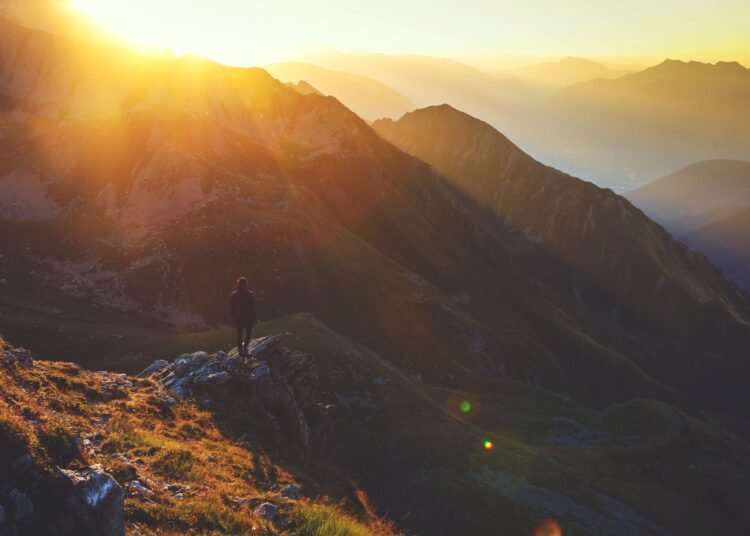 A lone hiker on a rocky mountain ridge at sunrise