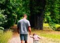 A father and child walking hand in hand down a forest path