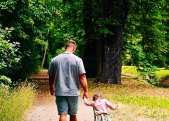 A father and child walking hand in hand down a forest path