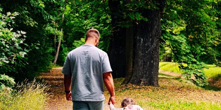 A father and child walking hand in hand down a forest path