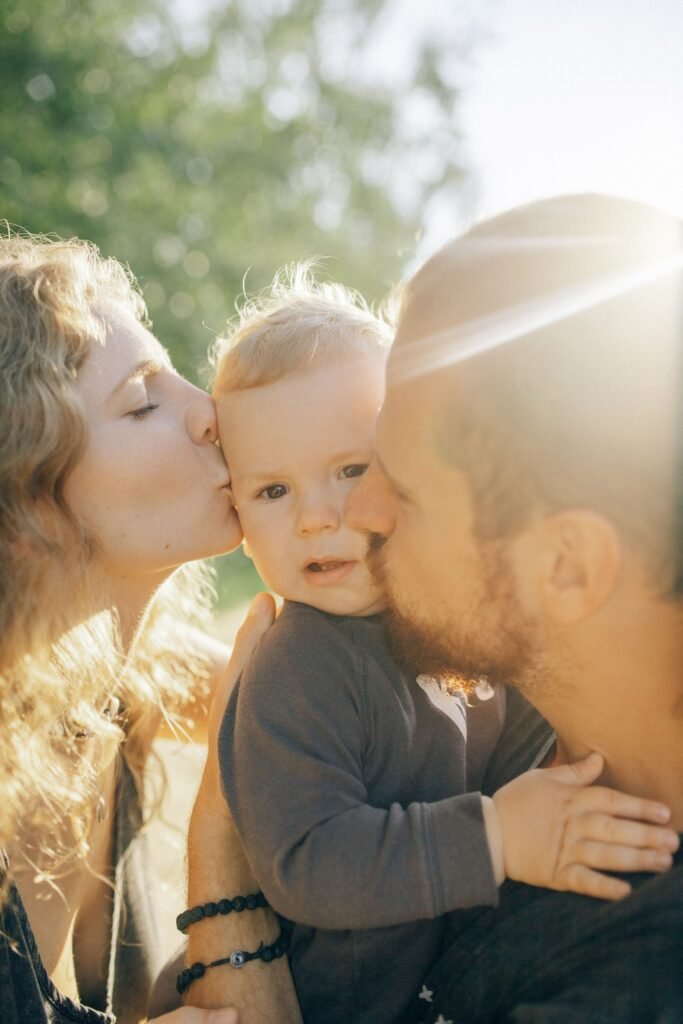 Parents kissing their baby in warm sunlight, Positive Phil